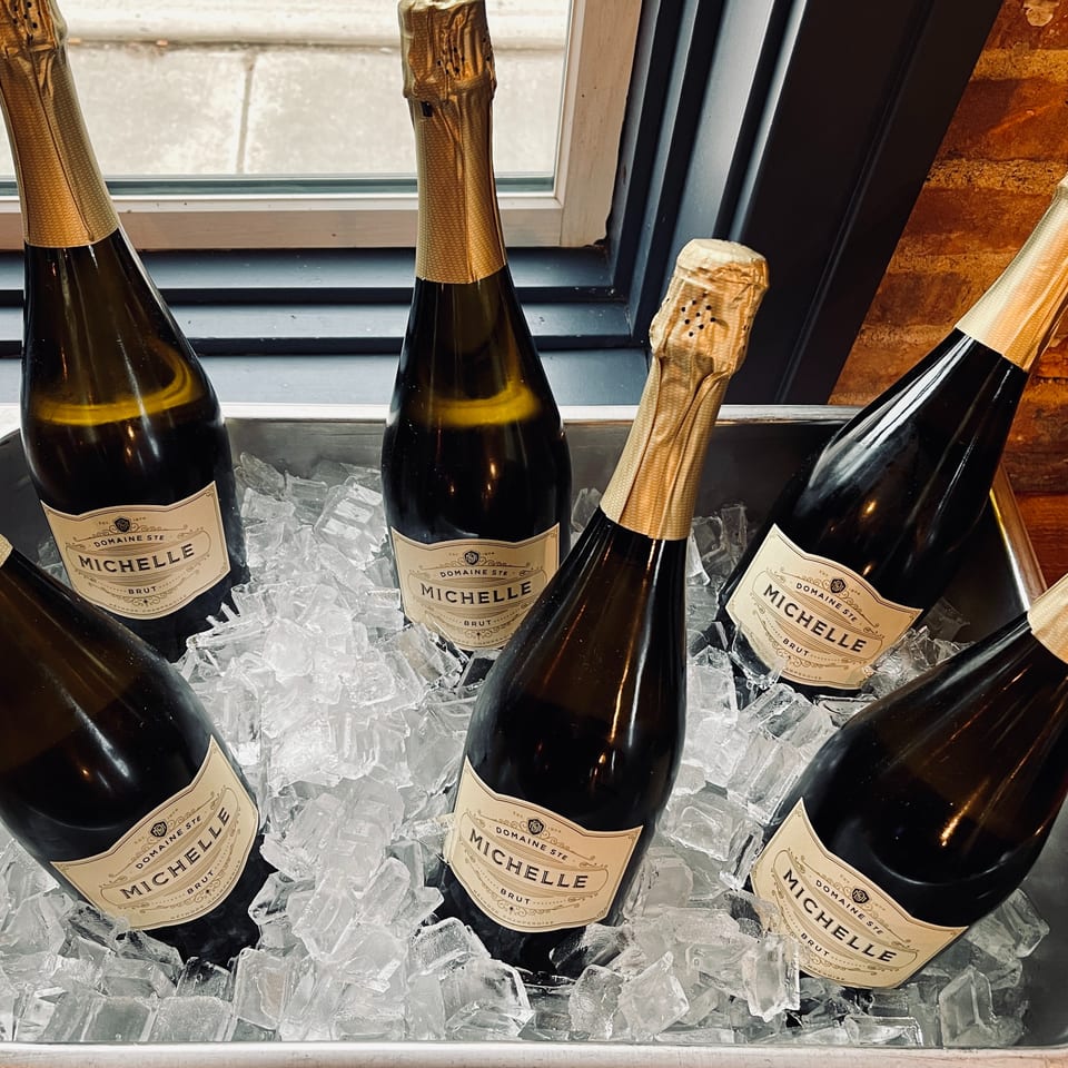 Six bottles of Domaine Ste. Michelle Brut sparkling wine chill in a metal tray filled with ice.