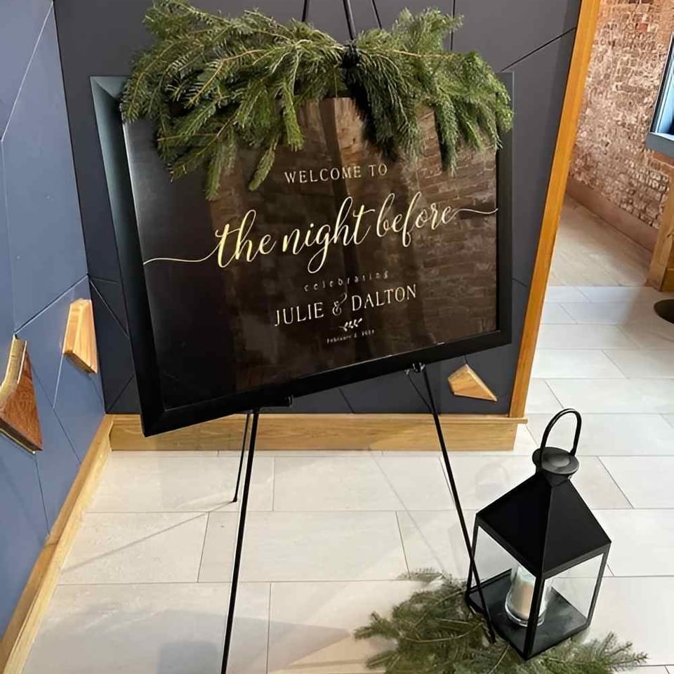 Welcome sign for The Night Before wedding event at Julie & Dalton, decorated with greenery and a black lantern.