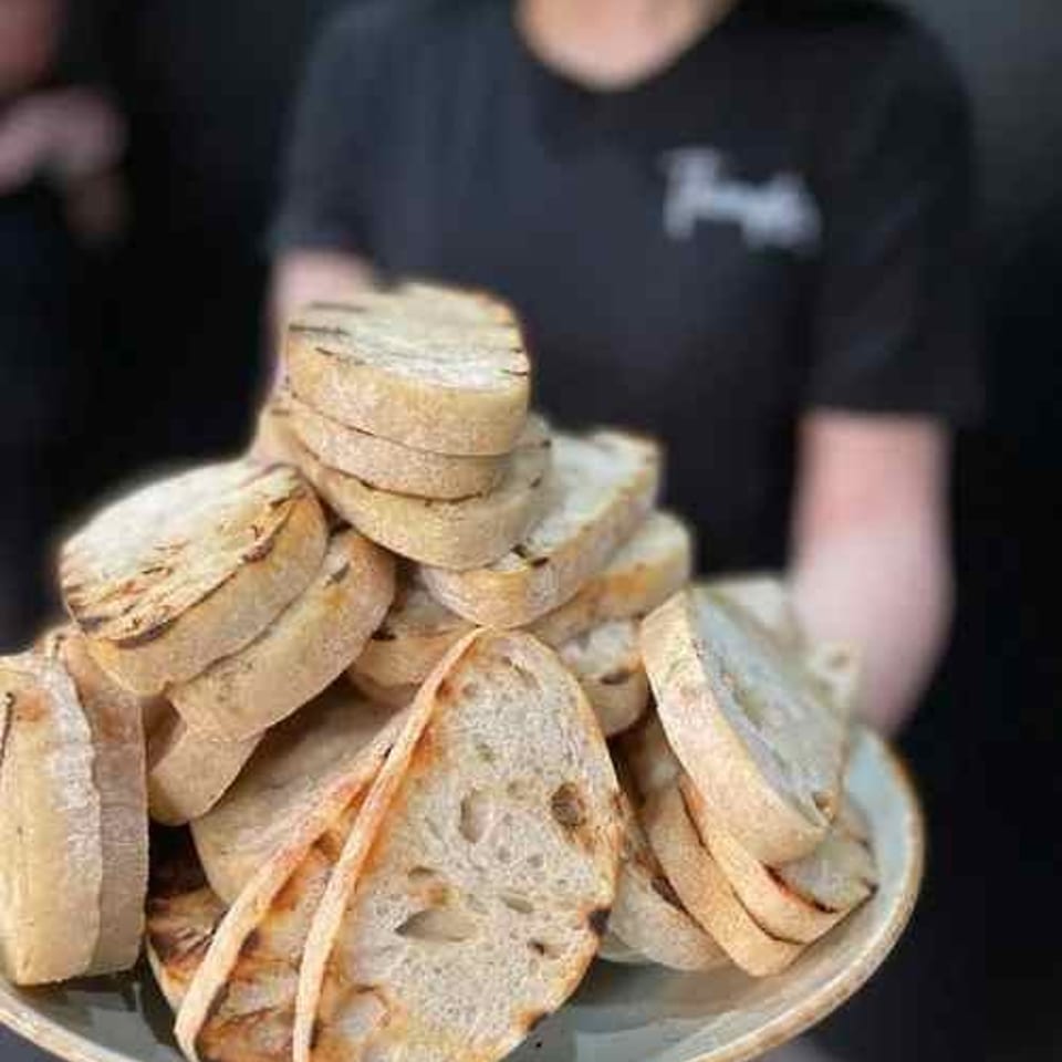 Server holding a large plate piled with sliced toasted bread in a restaurant.