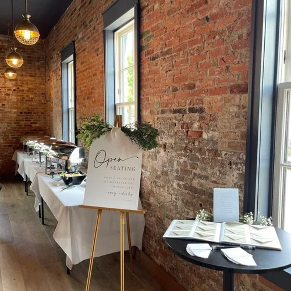 Brick-walled restaurant dining room with pendant lights, window-side tables, buffet setup, and an open seating sign.
